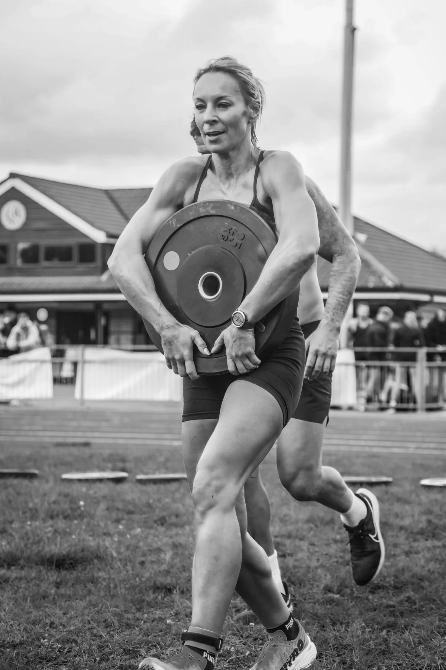 Sportler, der eine Hantelscheibe vor dem Körper trägt (Front Carry Labour)