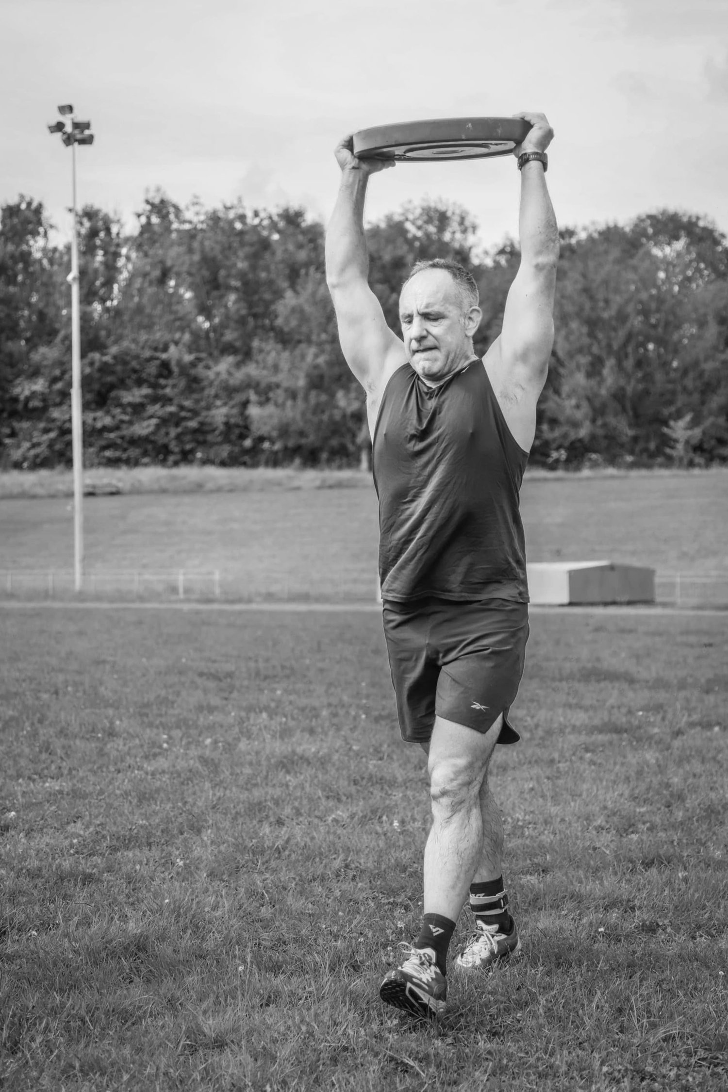 Sportler, der bei der Übung „Overhead Carry Labour“ eine Hantelscheibe über dem Kopf trägt